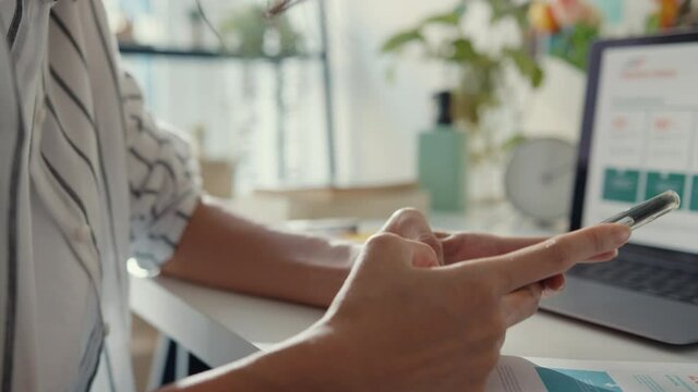 Close-up young asia lady freelance focus mobile phone chat with colleagues work finance graph account chart market plan in laptop at home. Girl student learn online at house, Work from home concept.