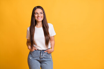 Photo of attractive cheerful lady look stand empty space hold hands pockets good mood isolated on yellow color background