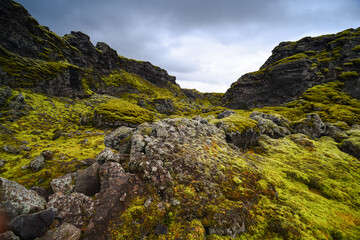 Ominous volcanic landscape and heavy clouds on a trail near Tjarnargígur crater pond, and through the bright green moss-covered crater row and lava fields of Lakagígar, Iceland	
