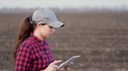 A woman farmer walks across field, works with tablet computer. An agronomist with tablet in his hands checks the field. Environmentally friendly agriculture. Modern digital technologies in agriculture
