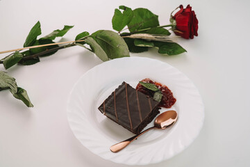 Una porcion de tarta de chocolate con mermelada de fresa y una rosa en la mesa