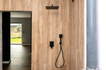 Black, matt metal concealed shower faucet and large rain shower protruding from the tiled wall,...