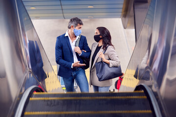Business Couple Commuting Riding Escalator At Railway Station Wearing PPE Face Masks In Pandemic