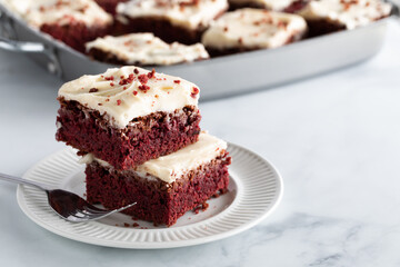 Two red velvet squares in a stack on a plate with other squares in soft focus in behind and copy...