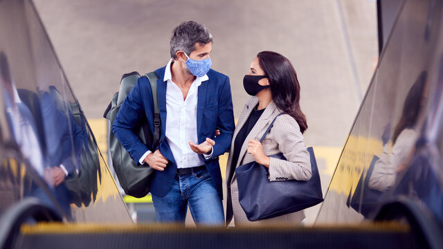 Business Couple Commuting Riding Escalator At Railway Station Wearing PPE Face Masks In Pandemic - Powered by Adobe