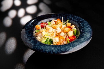 Fresh caesar salad with grilled chicken in a served plate on a black background.