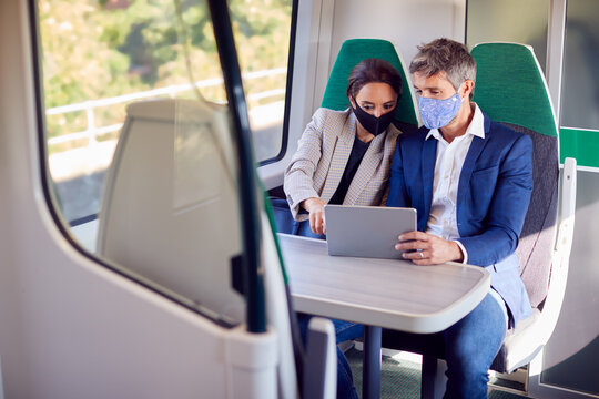 Businesswoman And Businessman On Train Using Digital Tablet Wearing PPE Face Mask During Pandemic - Powered by Adobe