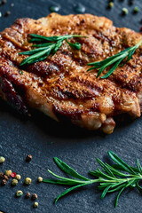 green rosemary and peppercorns lie near a cooked pork steak with layers of lard, on a wood board. meat hearty delicious. vertical shot