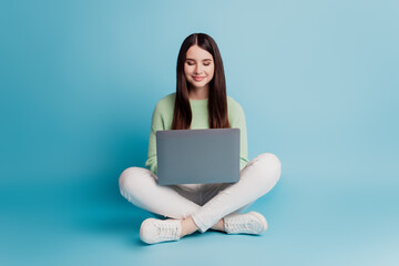 Naklejka premium Young happy woman sit legs crossed hold laptop isolated over blue background