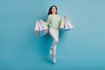 Young girl jump carry shopping bags isolated on blue background