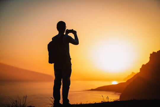 silhouette of a man holding a cellphone taking pictures outside during sunset in mountains