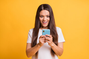 Photo portrait of amazed woman keeping smartphone using app smiling isolated on bright yellow color...