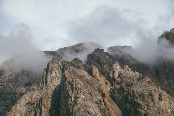 Scenic mountain landscape with great rocks in cloudy sky in vintage colors. Awesome sunny scenery with low clouds on rocky mountain top in pastel tones. Beautiful brown rock in sunlight and low clouds