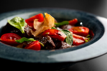 Salad with smoked beef and vegetables, sweet peppers and tomatoes on a gray plate on a black background.