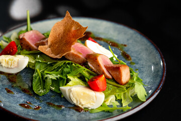 Meat salad with arugula and boiled egg on a gray plate on a black background. Restaurant menu.