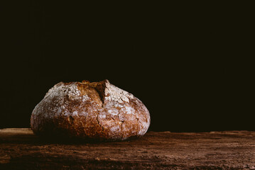 isolated rustic and golden round loaf of fresh whole grain bread on dark black background on top of...