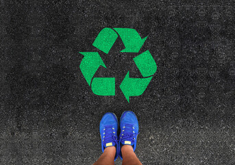 legs in shoes is standing next to recycle sign on road asphalt

