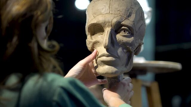 Woman sculptor at work on a sculpture of a human head.