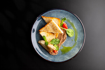 White bread toast, sliced with triangle and pate, decorated with spinach and cherry tomatoes on a gray plate on black.