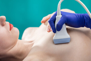A lady doctor using ultrasound is examining a young patient's breasts. Doctor's office. Close-up...
