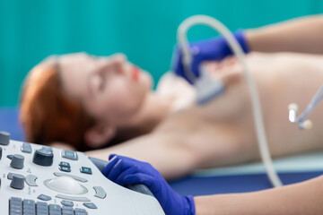 A patient is lying down and a lady doctor is examining her breasts with an ultrasound machine....