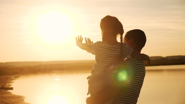 happy family dad and daughter by the sea at sunset silhouette. father and child kid reach out to the sun. kid a dream concept. happy family little girl and relax dad alone sunset with nature concept