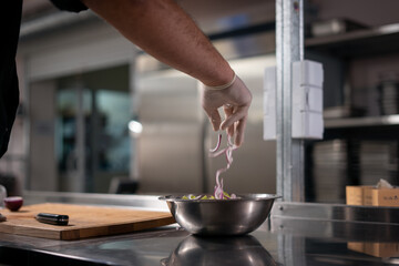 chef cook hands in gloves prepare salad and adding red onion in bowl at kitchen