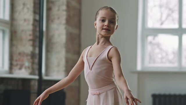 Tilt up shot of elegant caucasian 9-year-old ballerina in light pink dress posing to camera standing on her tip toes in pointe shoes practicing ballet dance
