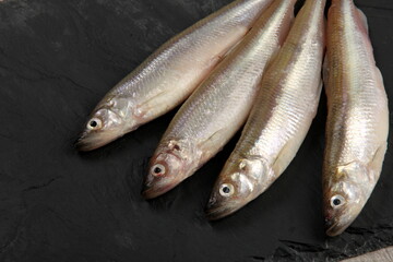 Fresh smelt fish on a black stone plate, Smelt fishes (European smelt) with lemon and green parsley, Group of fresh smelt fish 