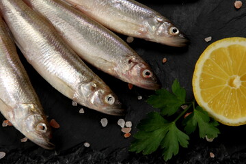 Fresh smelt fish on a black stone plate, Smelt fishes (European smelt) with lemon and green parsley, Group of fresh smelt fish 