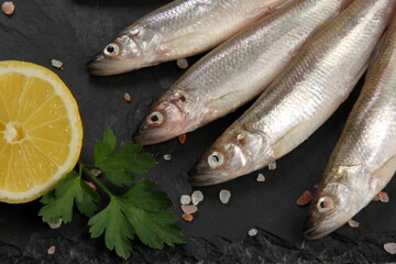 Fresh smelt fish on a black stone plate, Smelt fishes (European smelt) with lemon and green parsley, Group of fresh smelt fish 