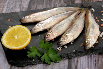Fresh smelt fish on a black stone plate, Smelt fishes (European smelt) with lemon and green parsley, Group of fresh smelt fish 