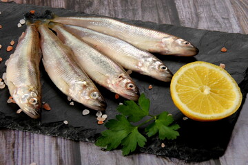 Fresh smelt fish on a black stone plate, Smelt fishes (European smelt) with lemon and green parsley, Group of fresh smelt fish 
