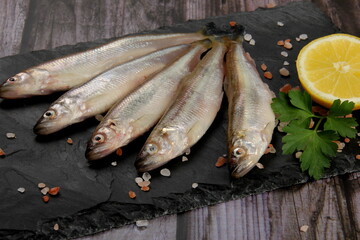 Fresh smelt fish on a black stone plate, Smelt fishes (European smelt) with lemon and green parsley, Group of fresh smelt fish 