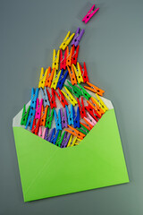 Conceptual composition, open green envelope and multi-colored clothespins on a gray background.