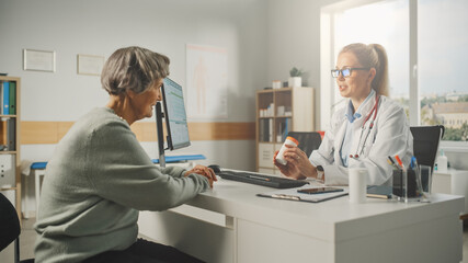 Obraz premium Female Family Doctor is Prescribing Drugs for Senior Patient and Speaking with Her During Consultation in a Health Clinic. Physician in Lab Coat Sitting Behind a Computer Desk in Hospital Office.