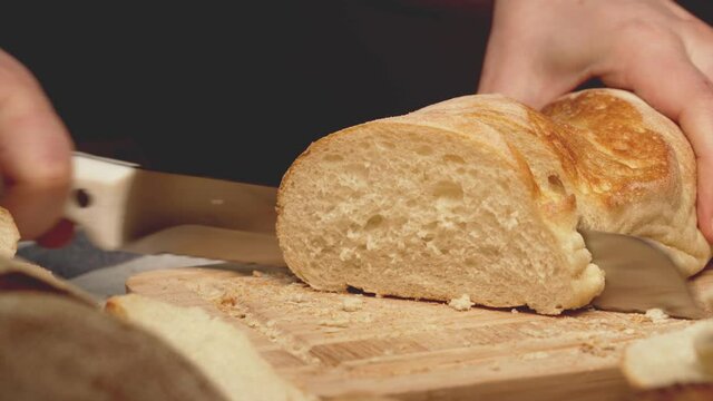 Hands of a woman cutting bread loaf on wooden cutting board