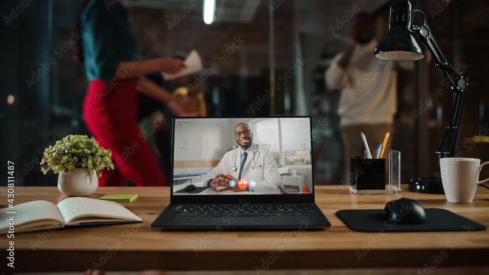 Poster shot of a laptop computer with portrait of a friendly male medical consultant having online video ca