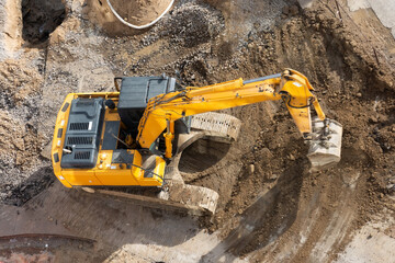 Excavator on the ground of a construction site with a raised bucket, top aerial view.