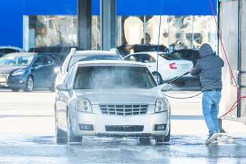Man washing his car with using a high compression pressure water jet. Washing his car in a self-service car wash station.