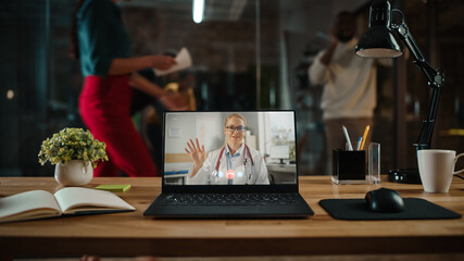 Fototapeta na wymiar Shot of a Laptop Computer with Portrait of a Friendly Female Medical Consultant Having Online Video Call. Computer on a Desk in a Busy Creative Office Environment. Authentic Hipster Agency Vibe. 