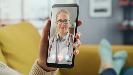 Close Up of a Female Chatting in a Video Call with Her Beautiful Female Family Doctor on Smartphone from Living Room. Ill-Feeling Woman Making a Call from Home with Physician Over the Internet.