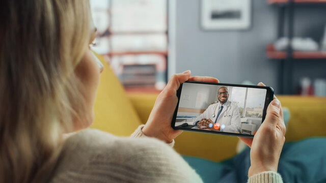 Close Up of a Female Chatting in a Video Call with Her Male Family Doctor on Smartphone from Living Room. Ill-Feeling Woman Making a Call from Home with Physician Over the Internet. Horisontal Vew.
