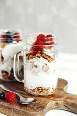 A healthy, dietary breakfast or snack of granola or oatmeal muesli with yoghurt and fresh wild berries. Ideal for vegetarians. Light background and vertical photo.