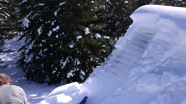 Slow motion shooting of a long haired young man shoveling a heap of fresh snow with blue hand shovel during a beautiful sunny winter day.
