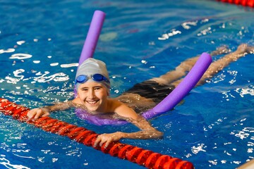 The boy in the pool learns to swim using a stick of foam. The child is fun and cheerful. Top view.