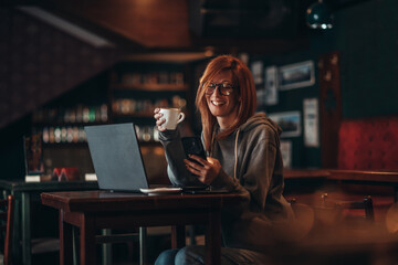 Woman using a laptop and a smartphone while drinking coffee in a cafe