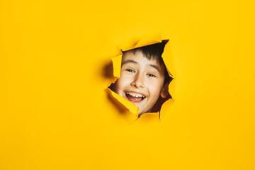 Cheerful happy face of child looking into hole in torn yellow paper wall. Sidebar for text, promotional information, advertising, positive news, events, sale, discount, best choice.
