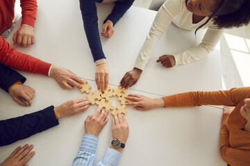 Close up of hands of multiracial office workers assembling wooden puzzles on desk symbolizing development and success. Concept of teamwork, business cooperation and the corporate community