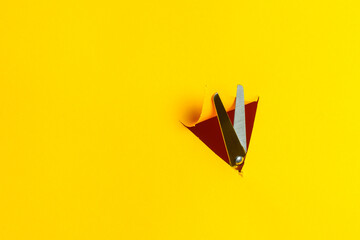 Scissors cut through a triangular hole in a yellow paper wall or cardboard sheet. Go through obstacles. Look the other way. Side view for text information.